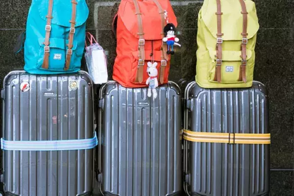 three suitcases along a wall with different coloured backpacks on top