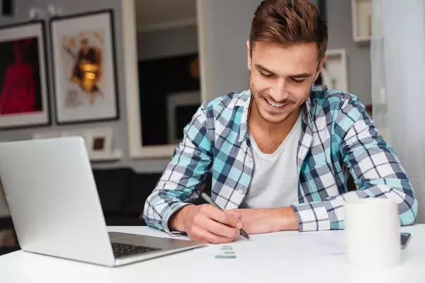 Smiling man filling out a form next to a laptop at home