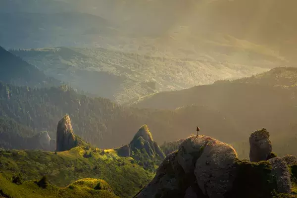 Man standing on top of a hill alone, overlooking a vast green landscape with no other people in sight
