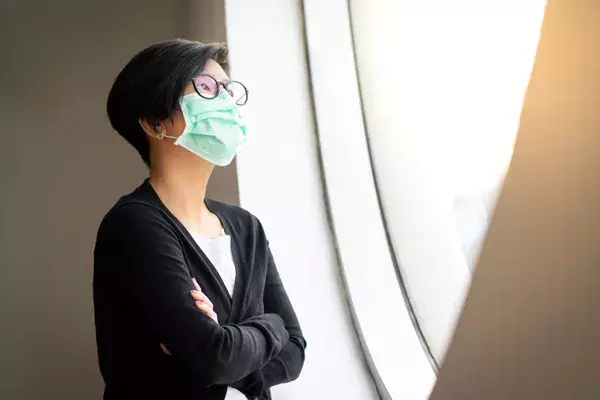 Asian woman wearing mask looking out of window