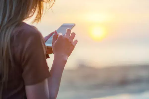 woman on beach looking at phone with sun setting in the background