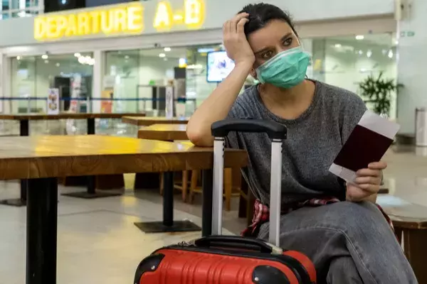 Overwhelmed passenger waiting in airport departures with suitcase