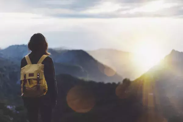 Woman with backpack watching sunrise at top of mountain
