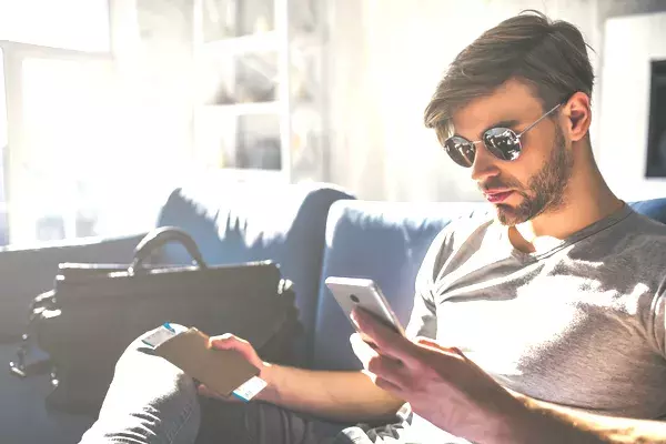 Man holding passport at home and reading message on his phone