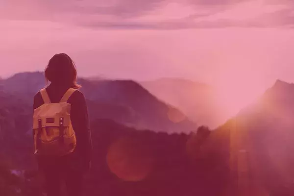 Woman with backpack watching sunrise at top of mountain