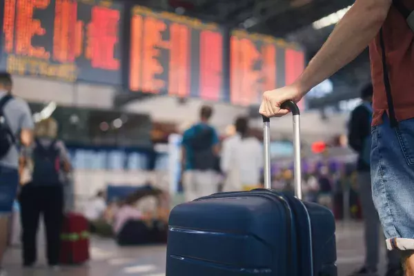 Person with suitcase in front of departure boards at airport
