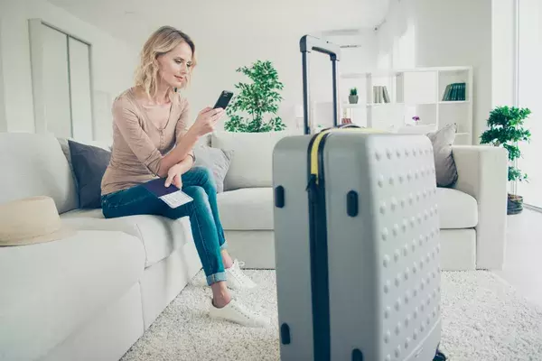 Woman sitting on the sofa looking at her phone besidea packed suitcase